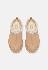 Hnedé semišové slip-on topánky s krémovým kožušinovým podšívkou a dekoratívnym aqua prešitím okolo goliera. Majú malý podpätok a logo.