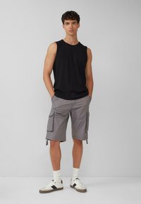 Schwarzes ärmelloses Top und graue Cargo-Shorts mit Taschen. Weiße Socken und Sneaker. Einfaches Design, lässige Passform und leichtes Material.
