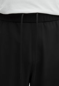 Sorte joggingsbukser med en glat, mat overflade. Har en elastisk talje med snor og en frontlomme.