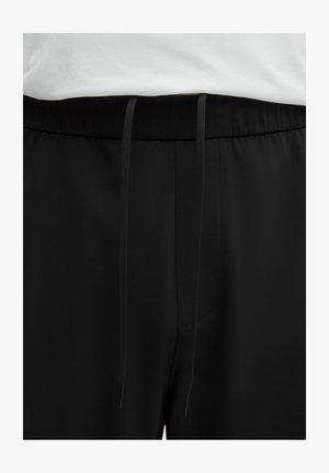 Pantalones de chándal negros con una textura suave y mate. Cuentan con una cinturilla elástica con cordones y un bolsillo frontal.