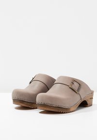 Sabots en cuir gris avec une large bande, détail de boucle à l'avant, semelle en bois et couture texturée le long de la base. Design à bout rond.