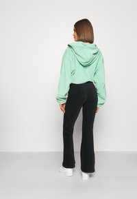 Mintgrøn hætte sweatshirt med en afslappet pasform, parret med sorte ribbede flagrende bukser og hvide sneakers. Bagfra, glat tekstur.
