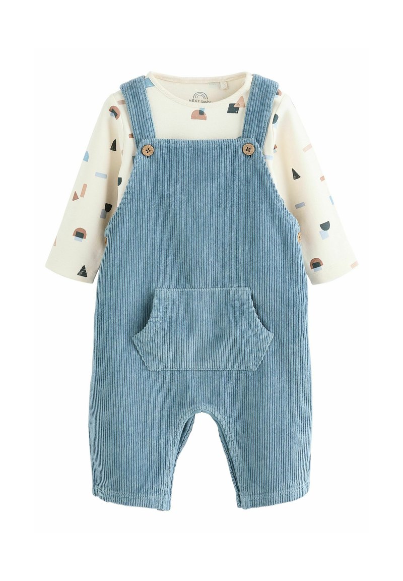 Blue corduroy overall with a front pocket and wooden buttons, layered over a cream long-sleeve shirt with a geometric pattern in pastel colors.