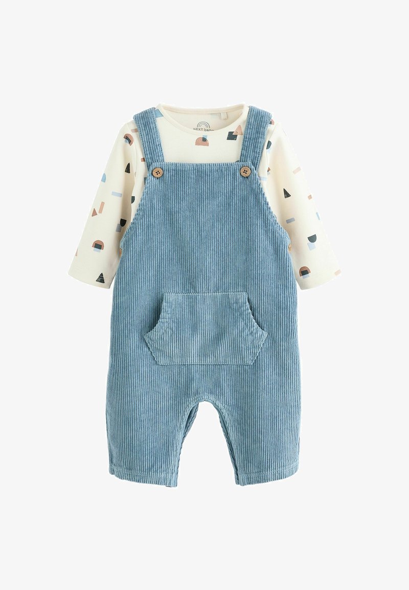 Blauwe corduroy overall met een voorzak en houten knopen, gedragen over een crèmekleurig longsleeve shirt met een geometrisch patroon in pastelkleuren.