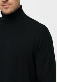 Fekete garbós pulóver puha kötött anyagból. Hosszú ujjaival és szoros nyakával rendelkezik. Egyszerű dizájn, minták vagy díszítések nélkül.