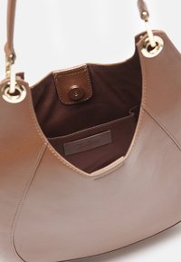 Ruskea nahkakäsilaukku, jossa on sileä pinta, kultaiset yksityiskohdat ja napsautuspainike. Sisällä on pehmeä kangaspinnoite ja logo.