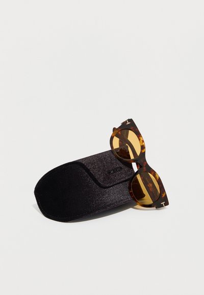 Γυαλιά ηλίου κατηγορίας cat-eye με καφέ-πορτοκαλί φακούς πάνω σε μαύρη θήκη προστασίας με υφή, σε λευκό φόντο.