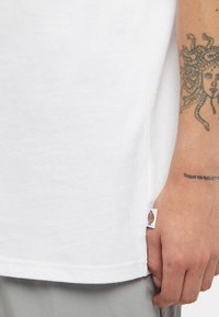 Hvid bomulds t-shirt med rund halsudskæring, der har et lille mærke ved sidesømmen. Stoffet er glat med en standard pasform.