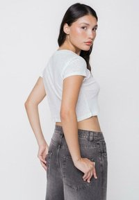 Camiseta blanca con corte corto y mangas cortas, que presenta una textura sutil, combinada con unos pantalones vaqueros de cintura alta en gris claro con bolsillos traseros.