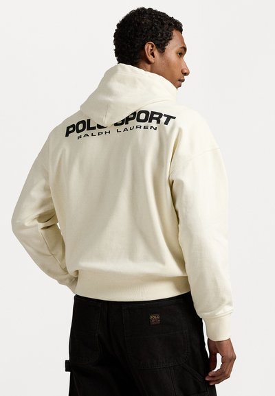 Krémová mikina s kapucí, která má na zádech velký černý potisk "POLO SPORT RALPH LAUREN". Ribovaná manžeta a spodní lem; měkká textilie.
