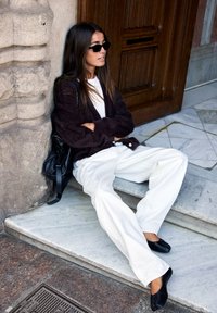 Svart, fluffig kappa över en vit skjorta, i kombination med vita vida byxor och svarta ballerinas. En svart handväska ligger bredvid.