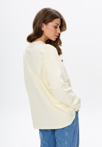 Oversized long-sleeve sweatshirt in soft pale yellow fabric, featuring a round neckline and dropped shoulders, paired with loose blue jeans.