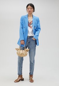 Blue double-breasted blazer, embroidered white T-shirt, light blue jeans, gold straw handbag with bow details, and brown studded heeled sandals.