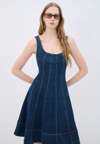 Denimmekko, jossa on tiukka yläosa ja liehuva hame, sinisestä kankaasta valmistettu, pyöreä pääntie ja näkyvät ompelusaumat.