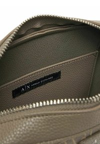 Interno di una piccola borsa in pelle beige con tasca con zipper e etichetta nera Armani Exchange cucita all'interno.