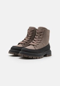 Bottoni da trekking marroni con uno upper in suede e suola in gomma nera. Presentano lacci robusti e battistrada testurizzati per una migliore aderenza. Logo impresso sul lato.