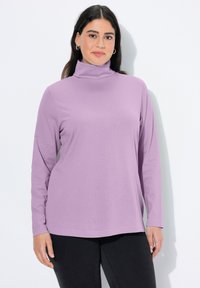 Fialový rolák s dlouhým rukávem z hladk�é látky s volným střihem. Má vysoký límec a zaoblený lem, doplněný tmavými kalhotami.