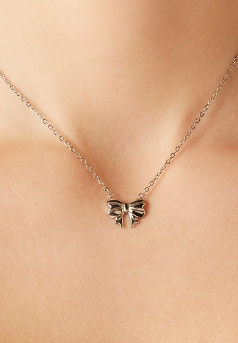 Zilveren ketting met een strikvormige hanger, met een gepolijste oppervlakte, fijne ketting en delicate details. Verstelbare lengte.