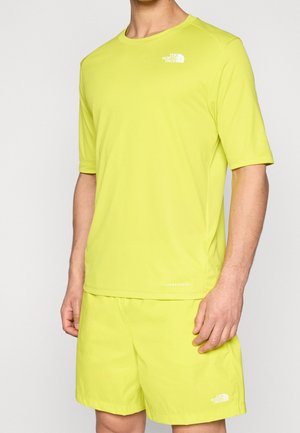 Homme portant un t-shirt The North Face jaune-vert vif à manches courtes et un short assorti sur un fond uni.