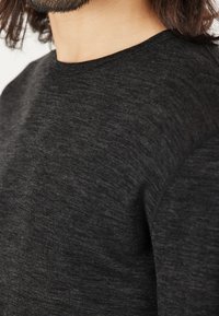Schwarzer Rundhals-Pullover aus strukturiertem Strickstoff, mit enganliegendem Design und glatten Ärmeln, das eine subtile Farbmischung hervorhebt.