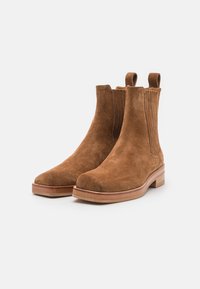 Botas de tobillo de ante marrón con paneles laterales elásticos, punta redondeada y un tacón de madera apilada para mayor soporte y estilo.
