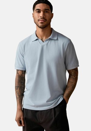 Lyseblåt polo-shirt lavet af blødt stof, med en V-halskrave og korte ærmer, parret med mørke bukser.
