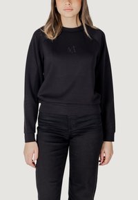 Felpa nera con scollatura rotonda, polsini e orlo a costine, caratterizzata da un sottile design "AL" in strass sulla parte frontale. Abbinata a jeans neri.