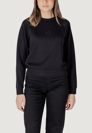 Felpa nera con scollatura rotonda, polsini e orlo a costine, caratterizzata da un sottile design "AL" in strass sulla parte frontale. Abbinata a jeans neri.