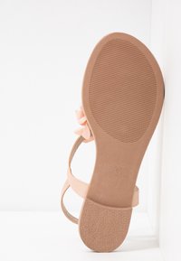 Nude strappy sandal with a textured rubber sole, featuring a soft pink flower accent, smooth leather straps, and a slim silhouette.