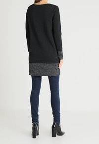Robe pull noire avec une coupe légèrement ample, dotée d'un ourlet et de manches texturés gris. Associée à un jean sombre et des bottines à talons.