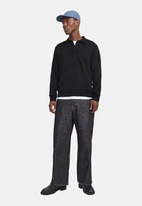 Sort pullover med et ensartet design, lange ærmer og krave, parret med løstsiddende mørke denim jeans og en lyseblå kasket.