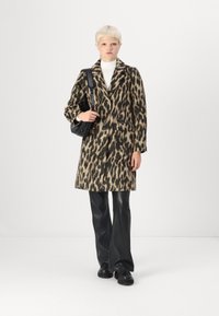 Abrigo de estampado de leopardo hecho de tejido texturizado, con un diseño de doble botonadura, solapas muesca y dos bolsillos frontales, llevado sobre pantalones negros.