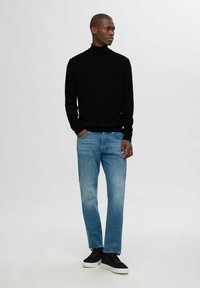 Svart polotröja, ljusblå denimjeans och svarta högstövlade sneakers. Klädseln har en enkel, modern design och en smal passform.