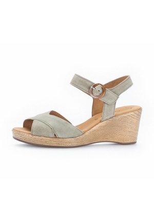 Green suede wedge sandals with cross straps and a circular wooden buckle, featuring a textured cork sole and open toe design.
