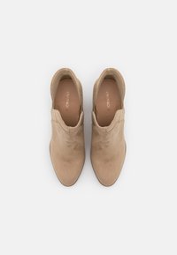 Stivaletti alla caviglia in suede beige con punta a punta e ritagli laterali. Presentano una texture liscia e un sottile logo del marchio sulla soletta.