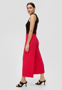 Plissé wijdvallende broek in felroze stof met een relaxte pasvorm en elastische tailleband, gecombineerd met een aansluitend zwart tanktop en zwarte hakschoenen.