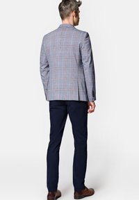 Szary marynarka w kratę z pomarańczowymi i niebieskimi akcentami, zestawiona z granatowymi spodniami. Posiada strukturalne ramiona i klasyczny krój. Brązowe skórzane buty.