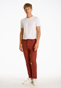 Röda slim-fit byxor i mjukt tyg, matchade med en vit t-shirt med kort ärm och vita sneakers. Inga synliga mönster eller accessoarer.