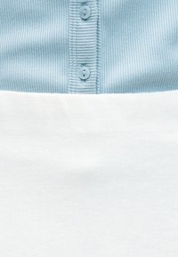 Ανοιχτό μπλε ριγέ ύφασμα με κάθετες γραμμές και δύο ομοιόμορφα κουμπιά πάνω από μια απλή λευκή υφασμάτινη επιφάνεια.