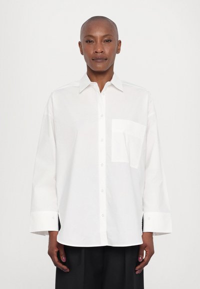 Chemise blanche à boutons, à manches longues, avec une poche poitrine unique et un col classique. Tissu lisse, coupe décontractée et sans motifs visibles.