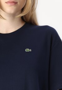 Navy blue cotton t-shirt with a round neckline and short sleeves, featuring a small green embroidered crocodile logo on the chest.