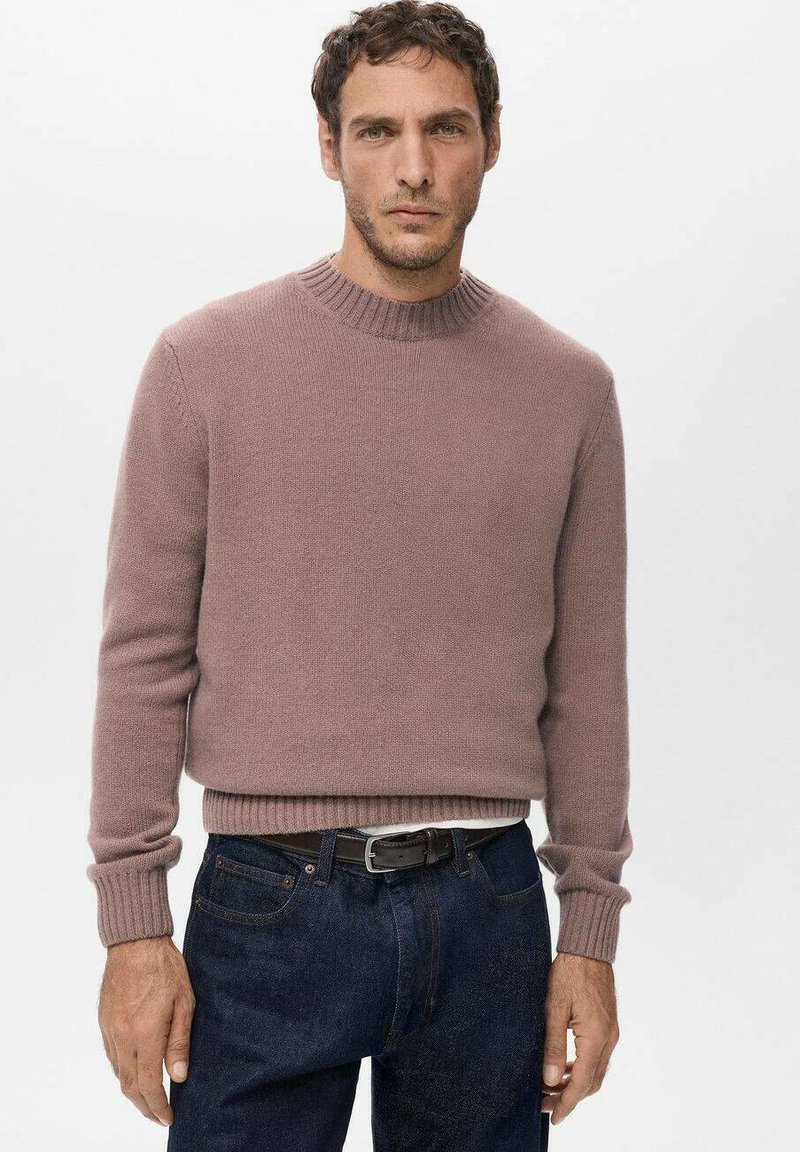 Dzianinowy sweter w kolorze zgaszonego różu z prążkowanym dekoltem i mankietami, o luźnym kroju i gładkiej fakturze, zestawiony z ciemnymi jeansami.