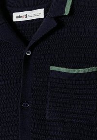 Cardigan en maille texturée bleu marine avec boutons, une poche poitrine bordée de vert et un col à bordure verte, taille 5-6 ans.