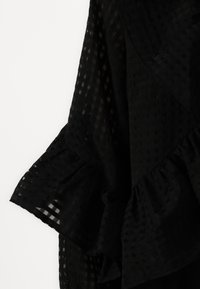 Svart lagdelt topp med volangerm, med rutedesign og gjennomsiktig tekstur, laget av et lett stoff.