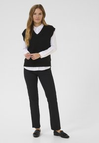 Black knitted vest with a v-neck, worn over a white collared shirt, paired with black straight-leg pants and black loafers. Simple design.