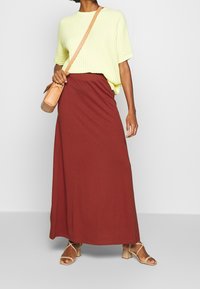 Gul tekstureret strikket kortærmet top parret med en lang burgunder jersey nederdel. Brune remsandaler med hæl og en lille tan crossover taske fuldender looket.