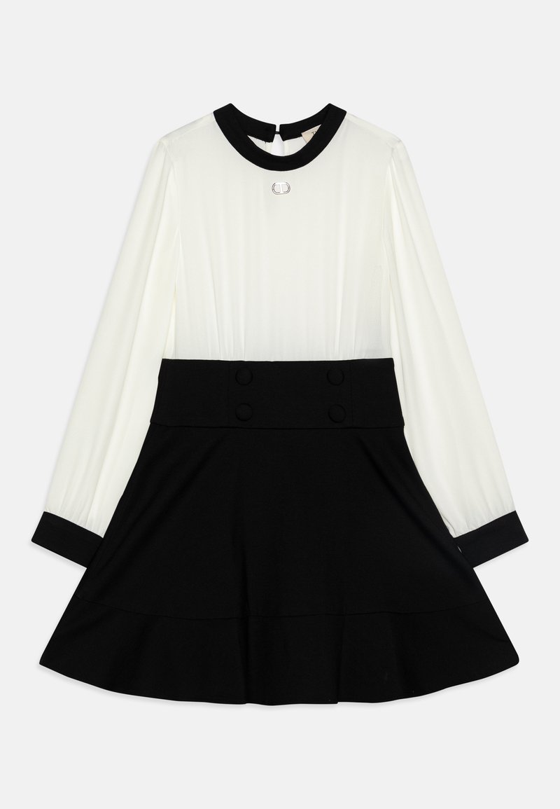 Robe à manches longues avec haut blanc, col noir et poignets noirs, ceinture noire avec boutons, et jupe noire évasée.