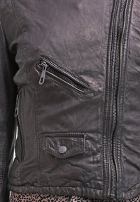 Sort læderjakke med en struktureret overflade, der har en skrå lynlås lomme, vertikal frontlynlås og en trykknap-lommeklap.