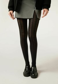 Collant neri a motivo con texture a trecce, abbinati a una gonna grigia. Indossati con mocassini neri con suola spessa.