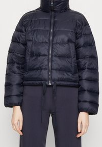 Tmavě námořnická prošívaná bunda s vysokým límcem, zapínáním na zip, nadměrným prošívaným vzorem, elastickým lemem a šňůrkami na stažení.